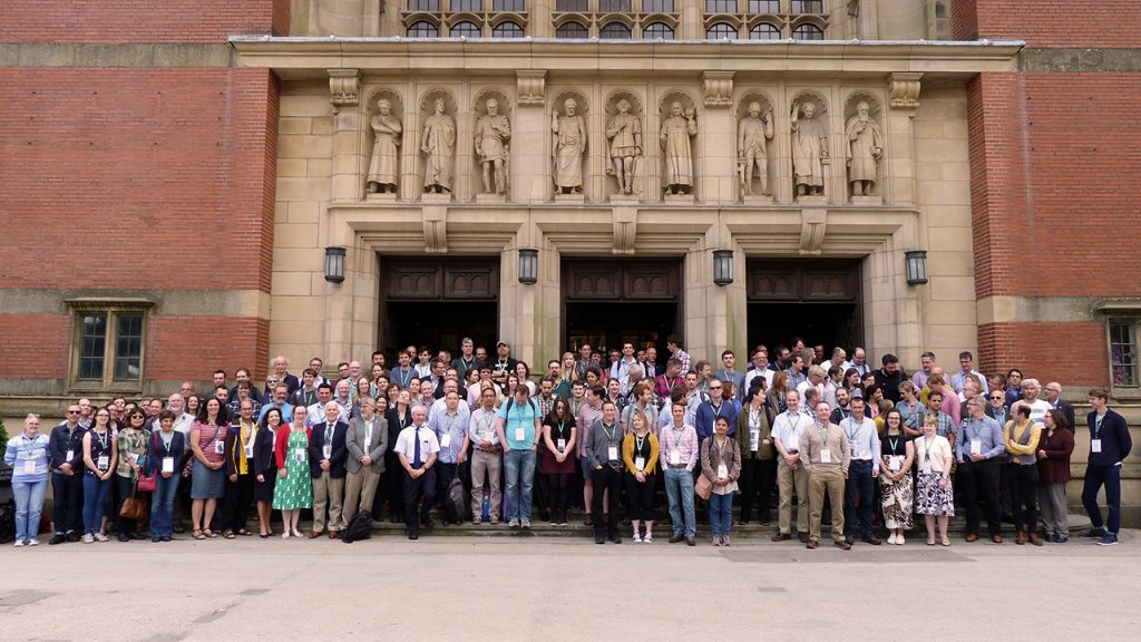 Two hundred staff stand in four rows, on stairs in front of a grand, red-brick building