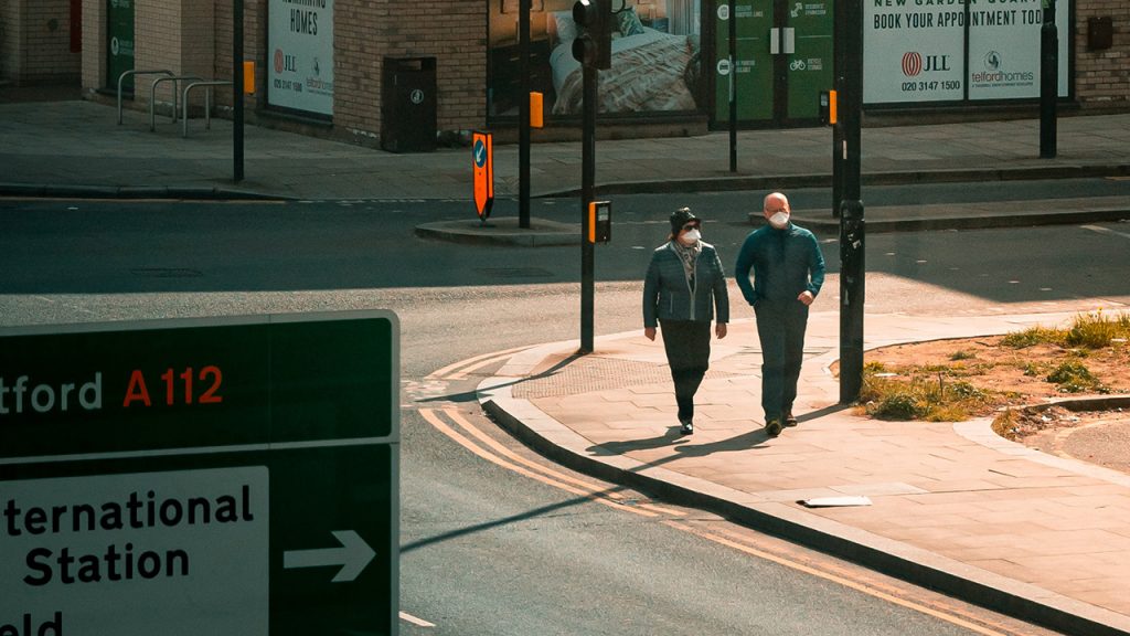 Male and Female walk along a pavement, both are wearing face masks.