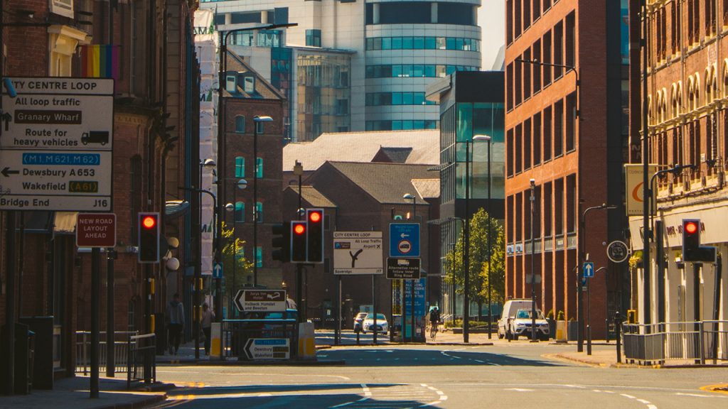 City centre road with large orange buildings on either side, traffic lights and signs are visible in the distance.