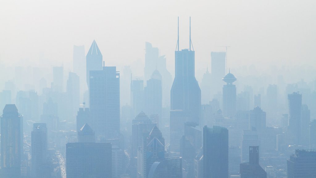 Large skyscraper buildings are silhouetted through a thick blue haze