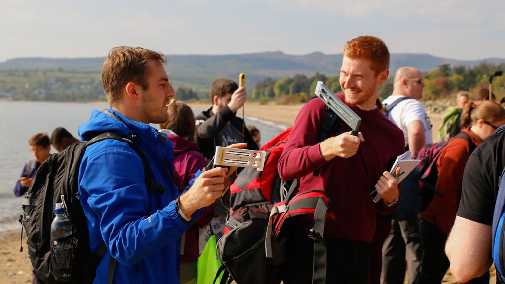 A group of students use wind measuring equipment on a beach