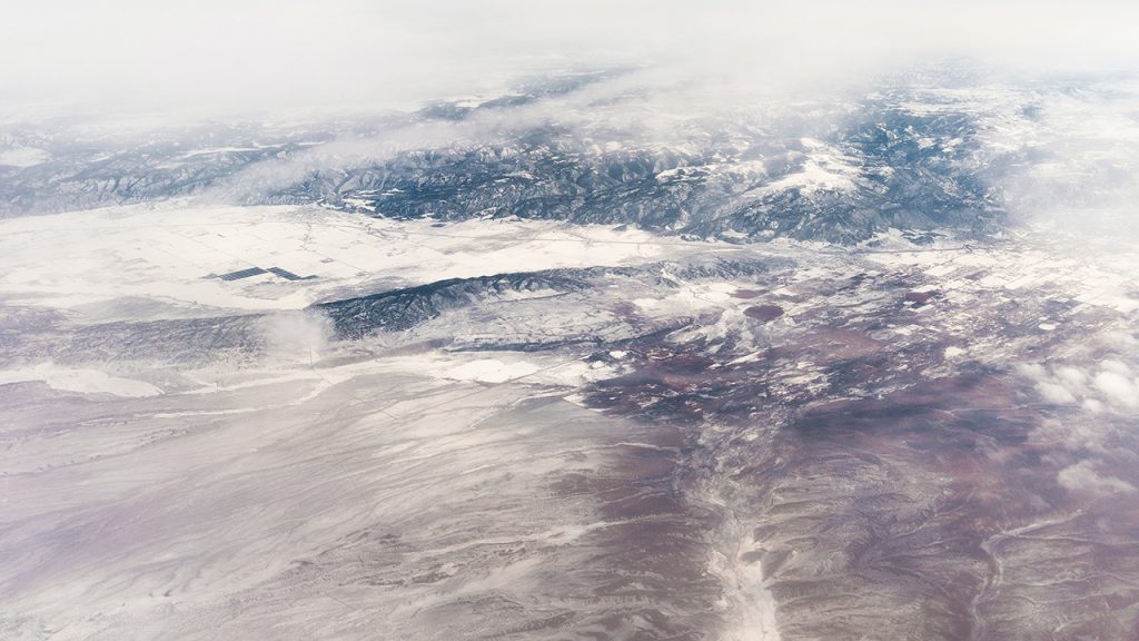 Semi-transparent layer of white cloud viewed from above, there is blue water and green land visible through the middle of the cloud.