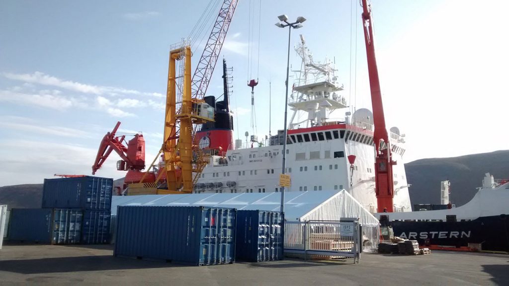 Red crane lifts blue shipping container onto white ice-breaker vessel