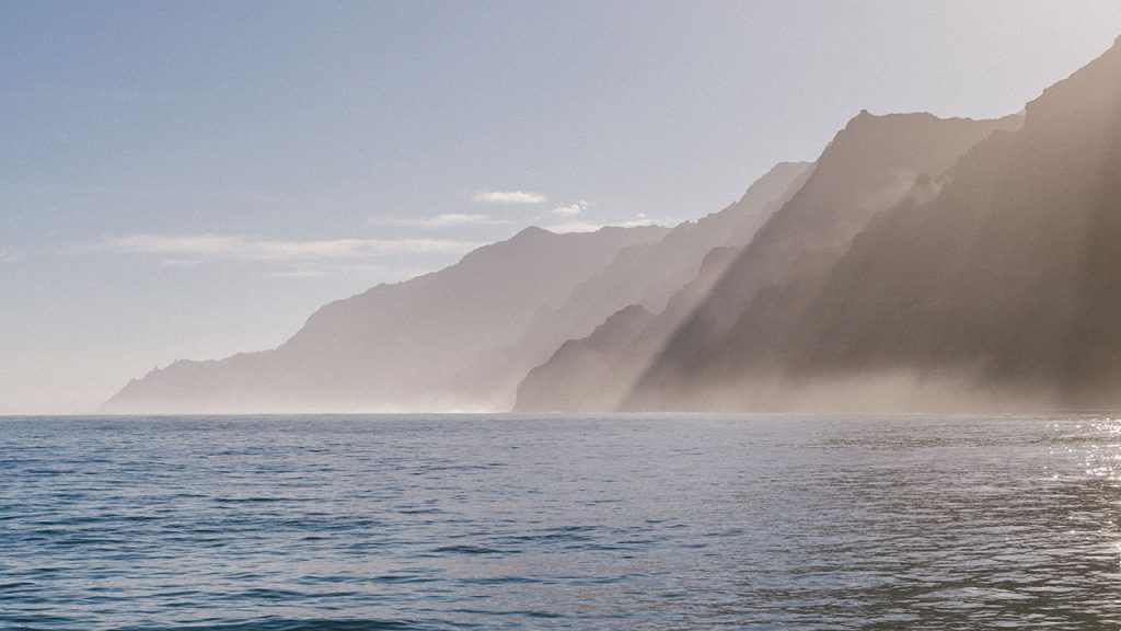 Mist rises off blue ocean, with sea cliffs in the distance