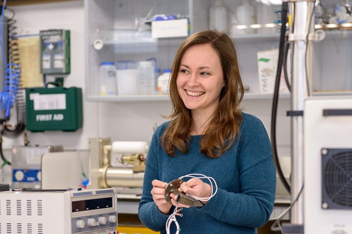 Brown haired woman wearing blue jumper holds cables in her hands in a laboratory