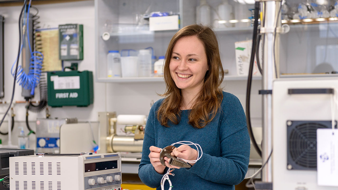 Brown haired woman wearing blue jumper holds cables in her hands in a laboratory