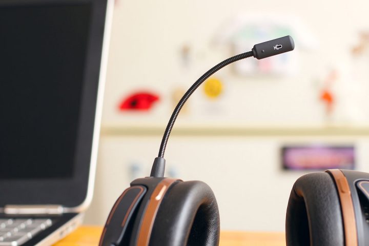 Black headphones with mouthpiece rest on a wooden desk, next to a laptop.