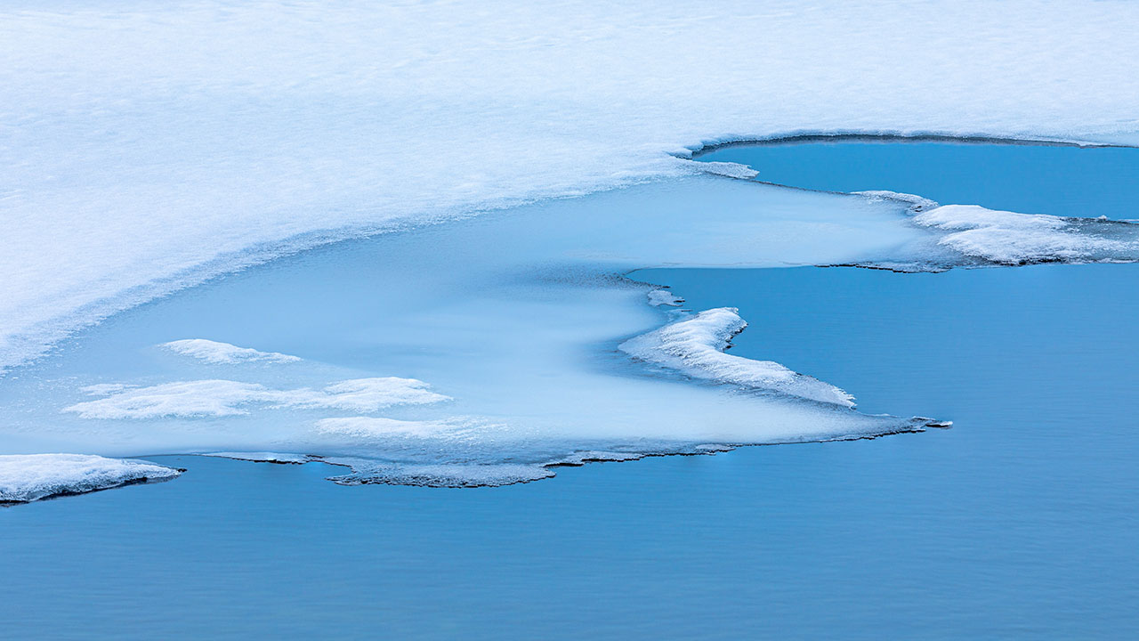 Large white sheet of ice sits on top of a blue body of water