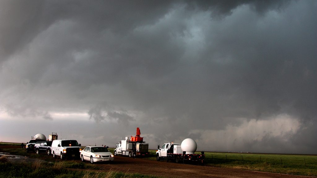White cars towing round, white radar equipment, in front of a dark, grey, cloudy sky.