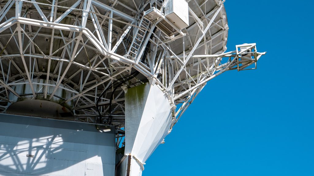 Large, structural metal work at the base of a large, white radar dish