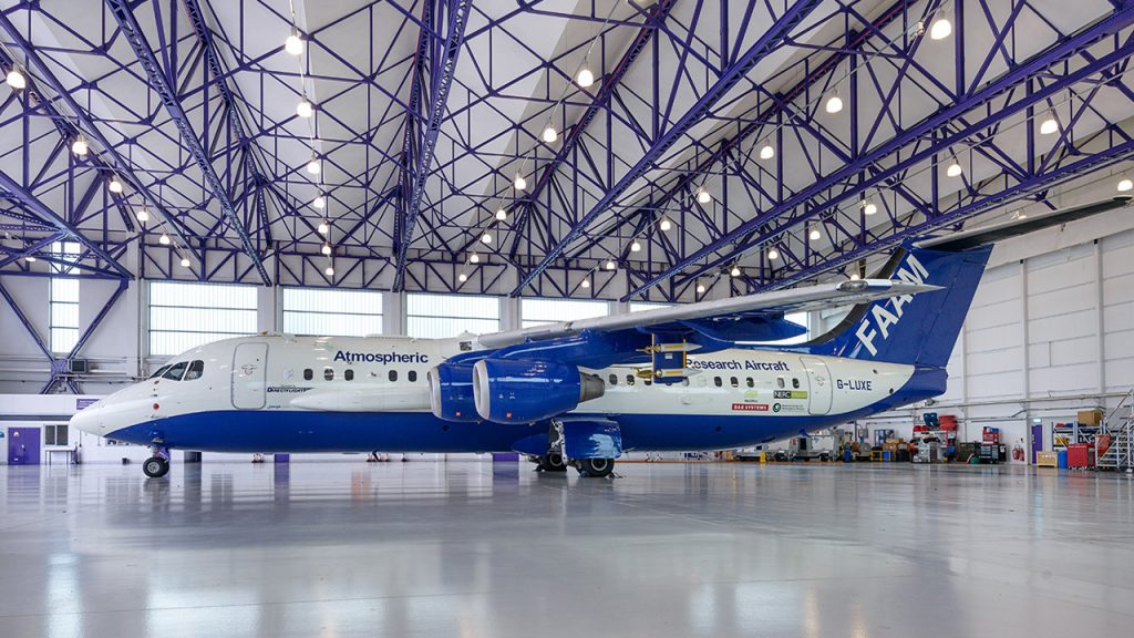A large blue and white aircraft is parked inside a hangar with a shiny grey floor