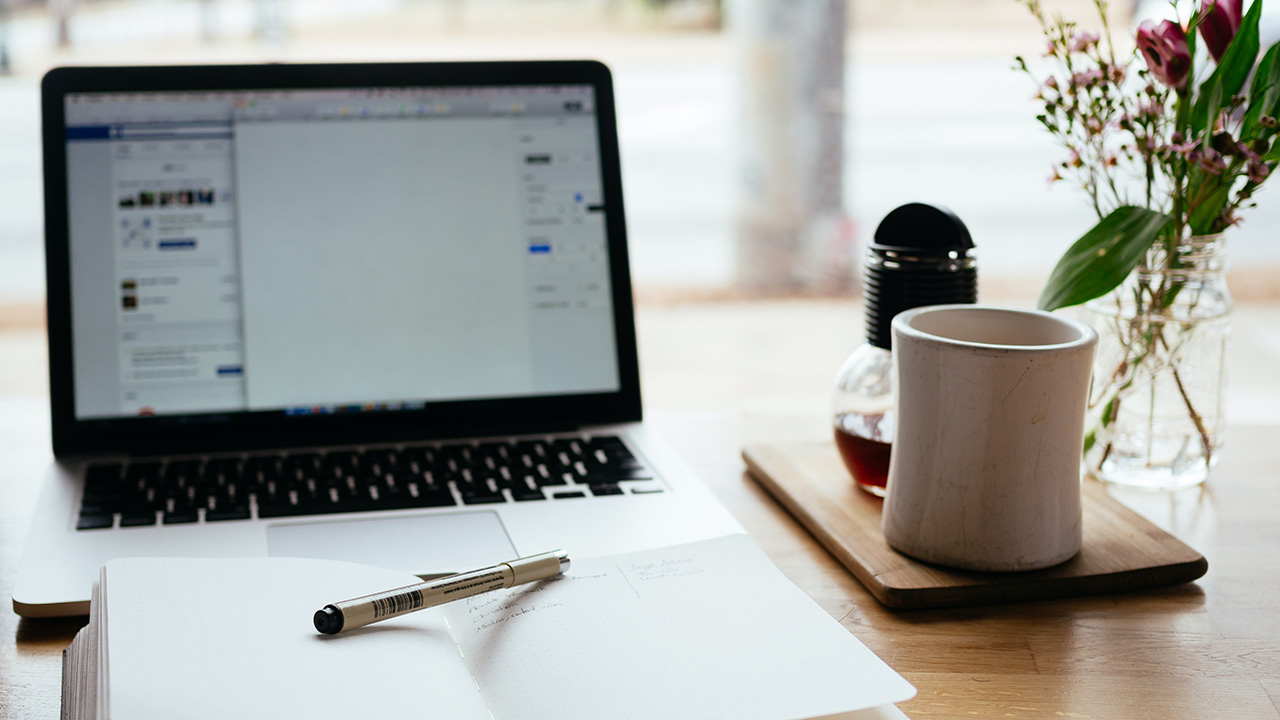 Notepad and pen, laptop, and mug on a desk