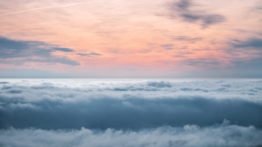 Pink sky above rolling, blue clouds