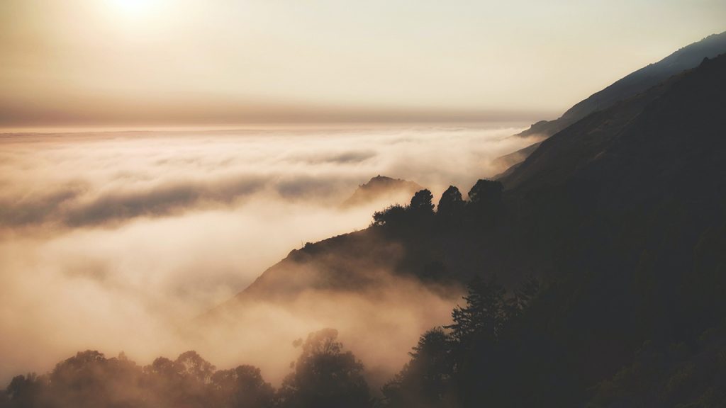 Low-lying clouds wrap around a dark hillside