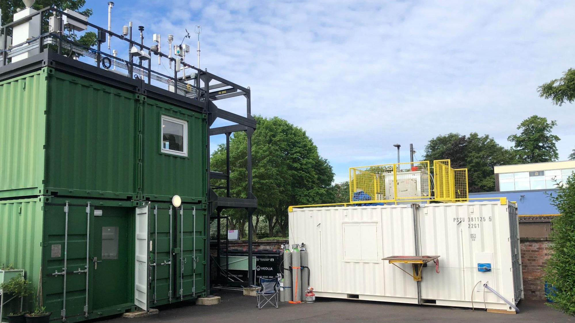 Three shipping containers adorned with scientific instruments below a blue sky.