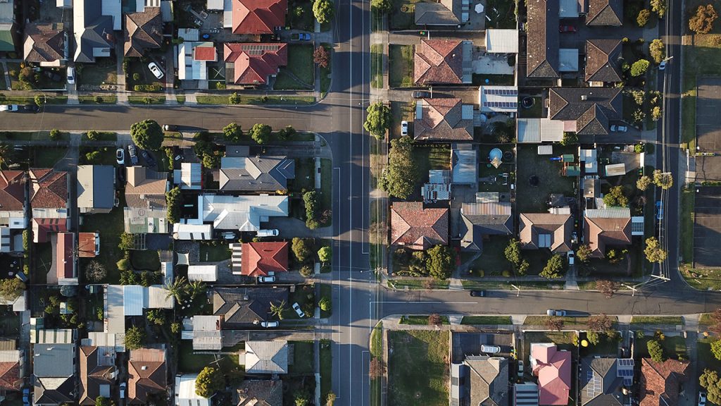 Aerial view of housing estate, showing red rooftops and grey roads.