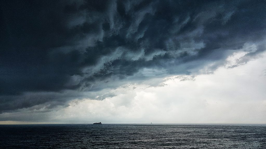 Large dark blue and grey storm cloud above a ship on the sea