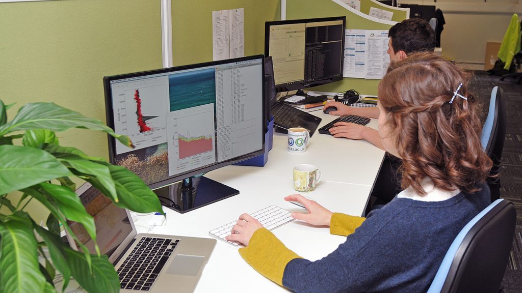 Person sits at desk, looking at data on computer screen