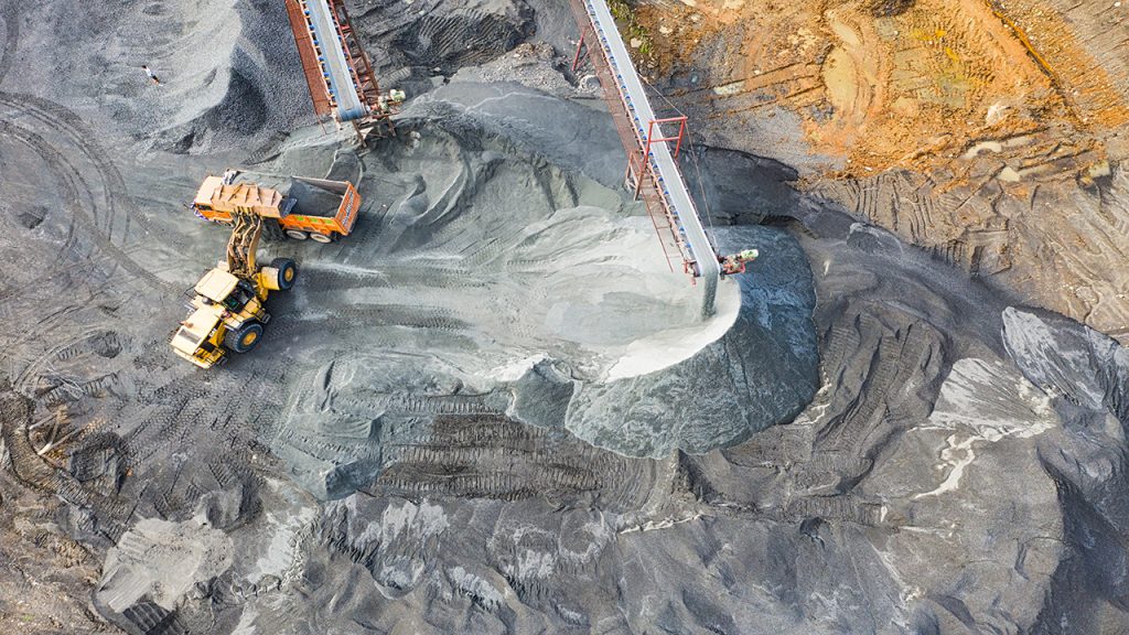 A yellow excavator moves dark grey coal from a pile into a truck