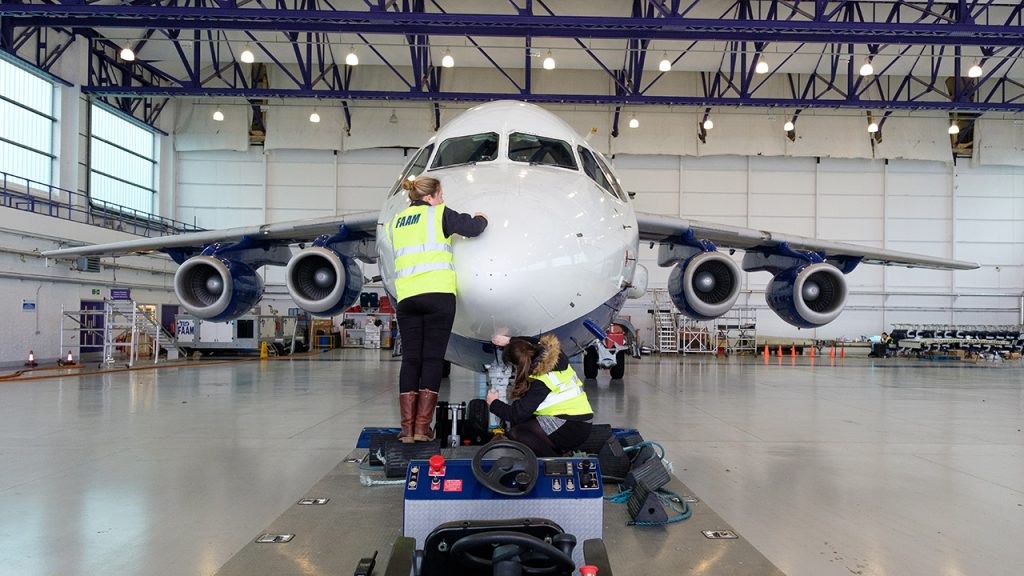 Two people wearing hi-vis jackets polish a large research aircraft nose