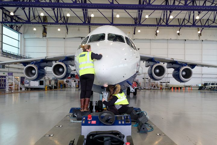 Two people wearing hi-vis jackets polish a large research aircraft nose