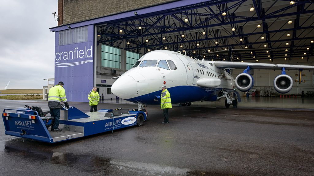 People wearing hi-vis clothing tow research aircraft out from large hangar