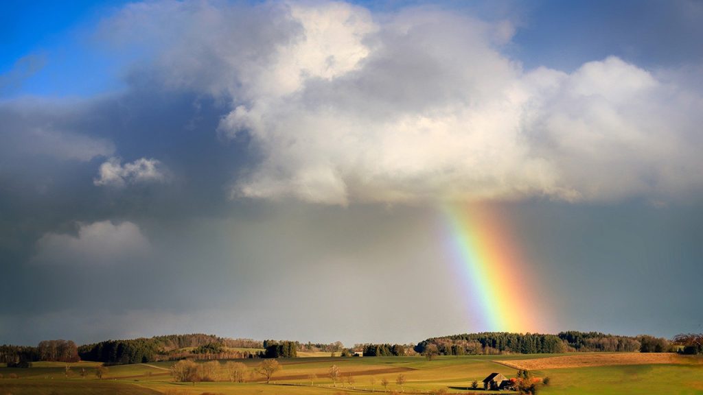 a cloudy sky with a rainbow above green fields