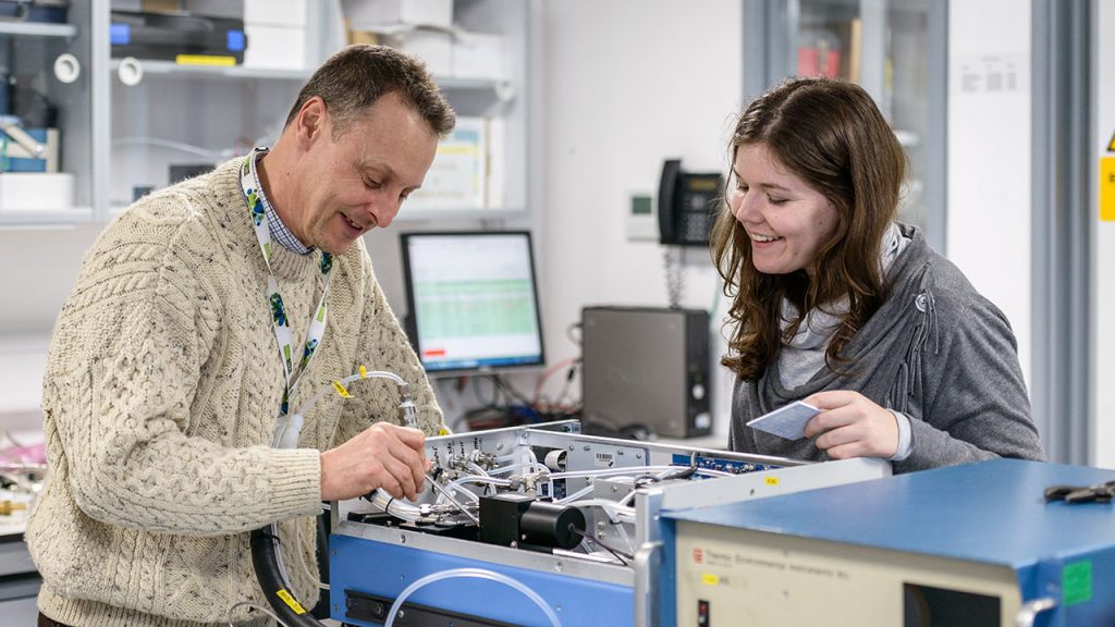 Two people work together on a scientific instrument in a laboratory