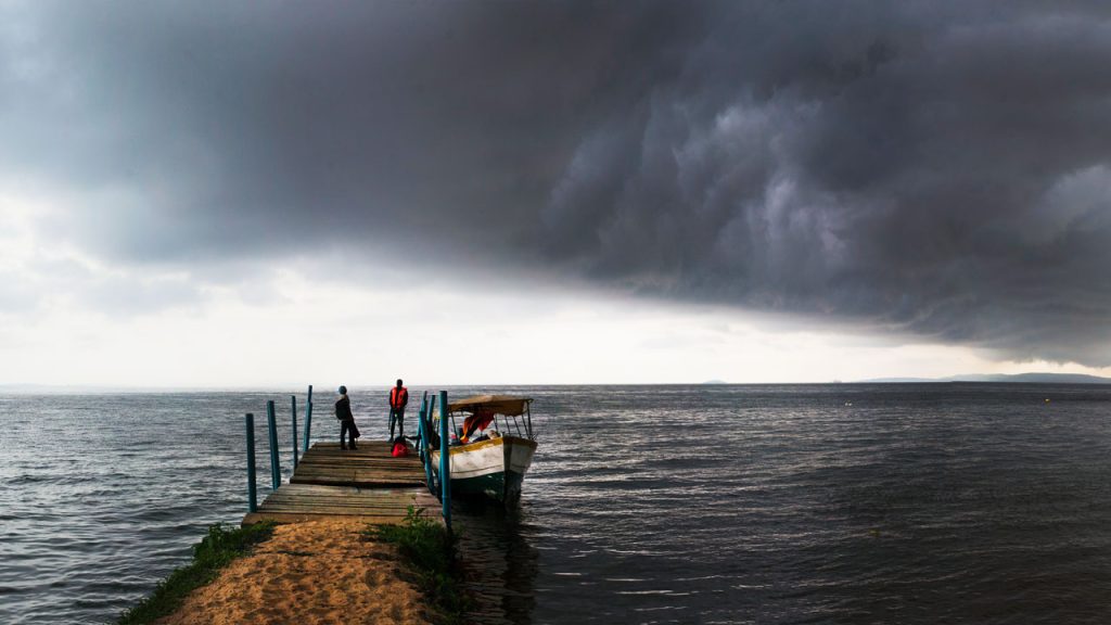 Two fisherman stand on edge of large lake in Uganda