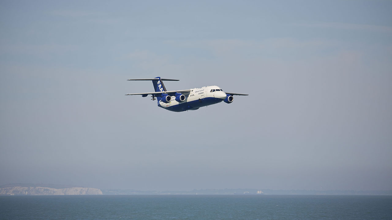 Blue and white research aircraft flying low over blue waters