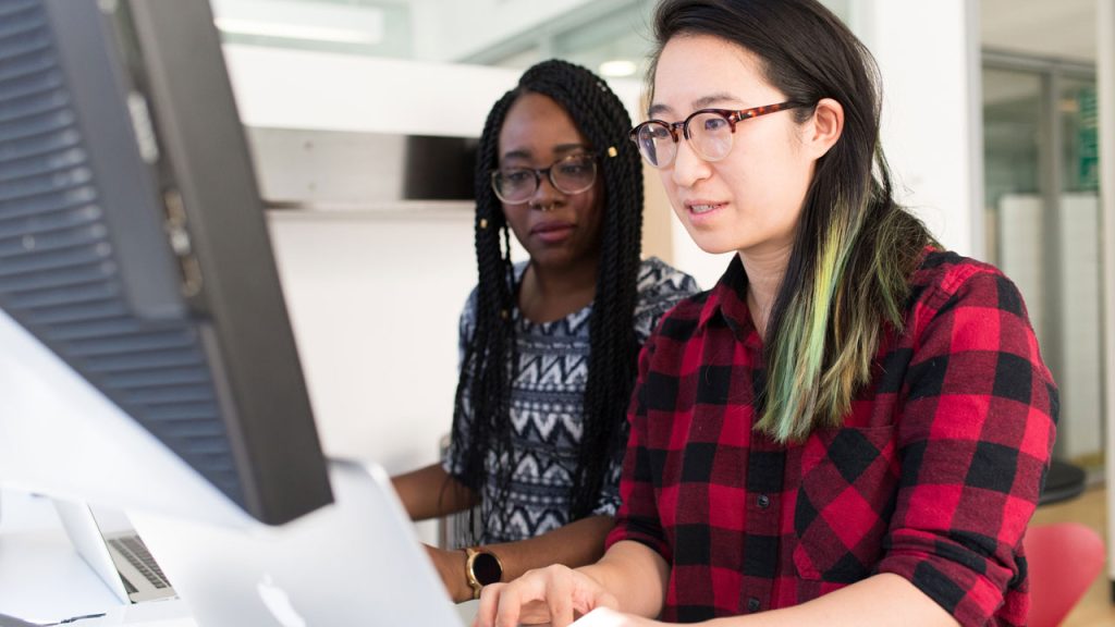 Two women sit at a computer screen