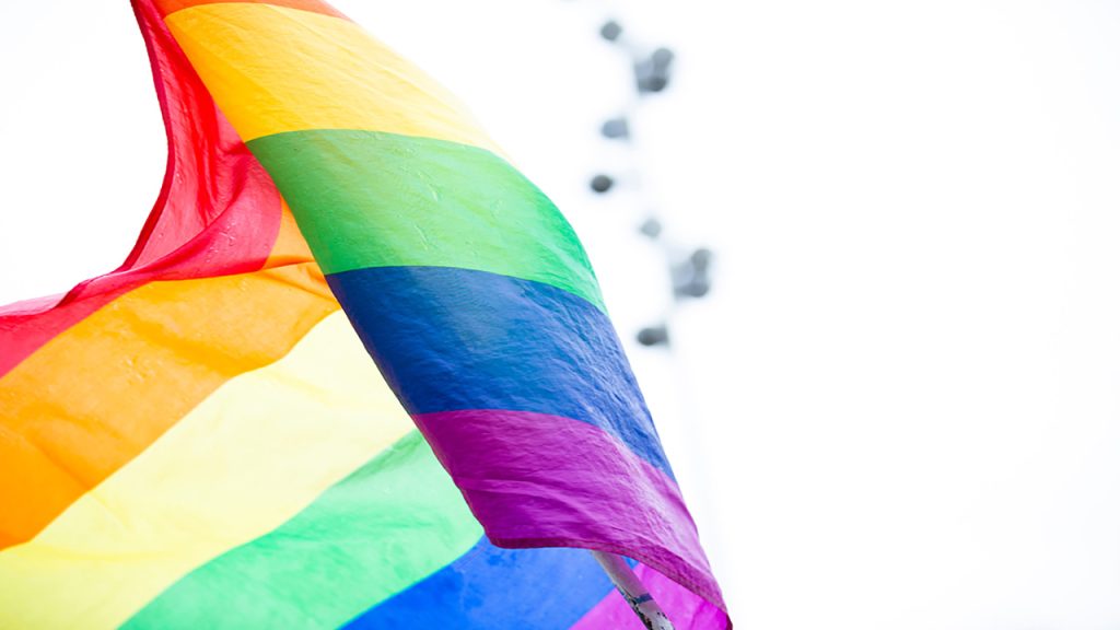 A flag with red, orange, yellow, green, blue and purple stripes waving in the air