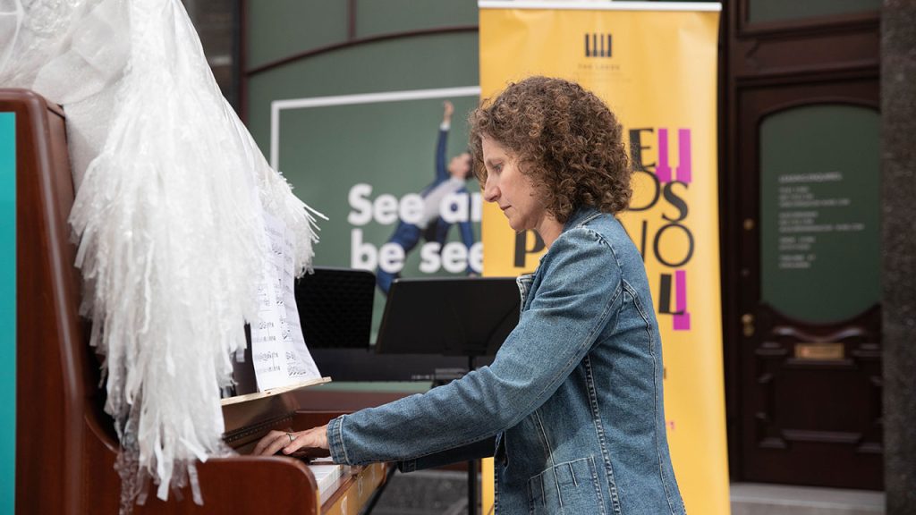 Pianist plays upright piano, decorated with a wave of white recycled plastic