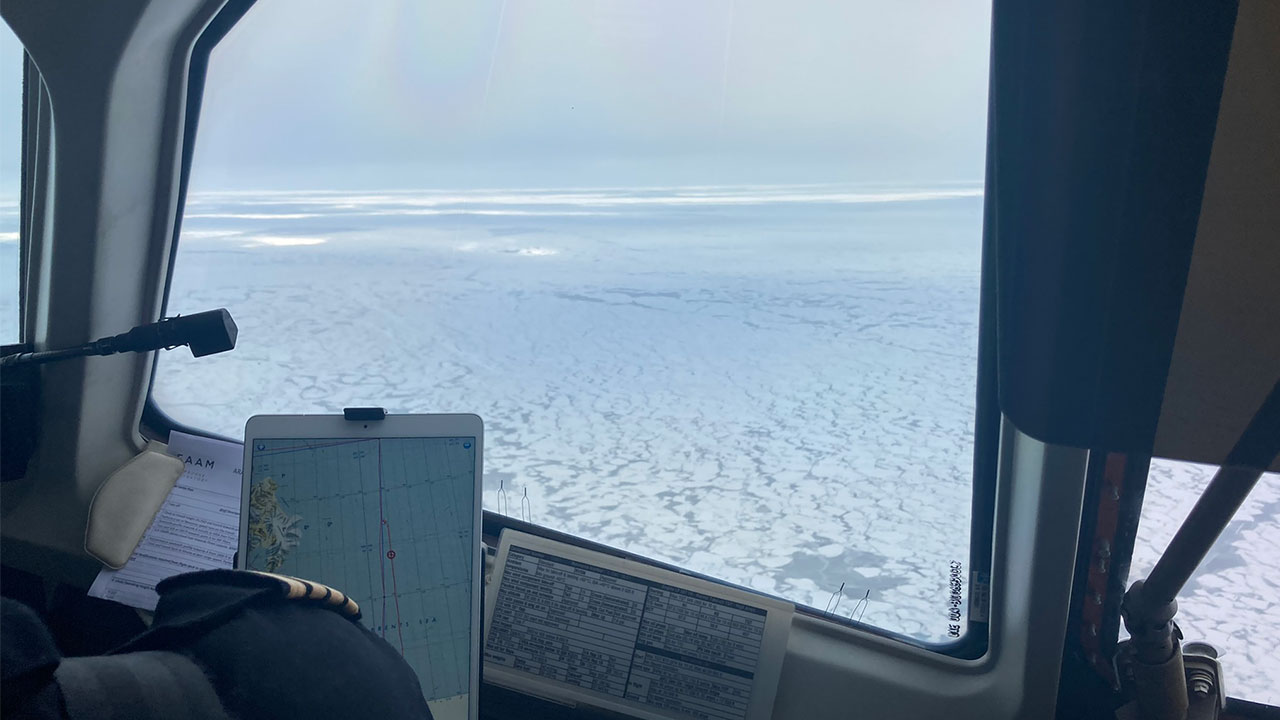 Pilot looks out aircraft window mid-flight, as it flies over Arctic sea ice.