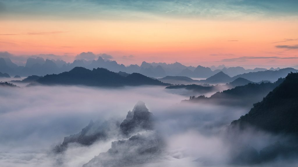 A sunset sky over dark mountains surrounded by low cloud and fog