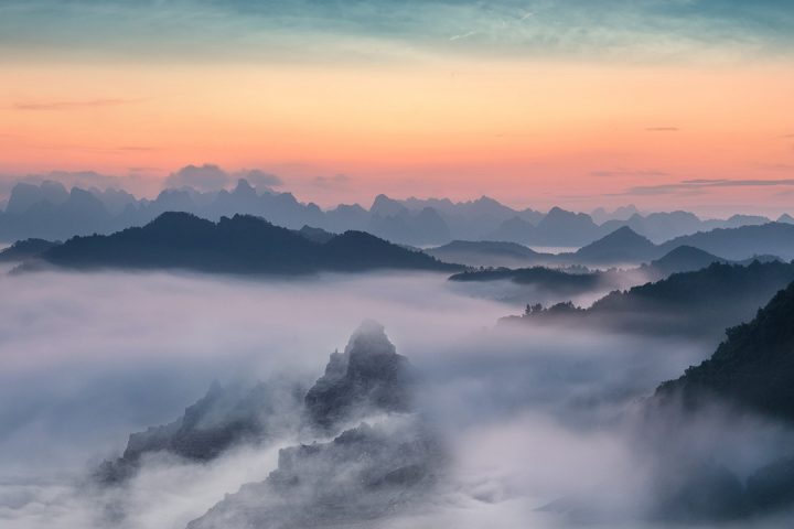 A sunset sky over dark mountains surrounded by low cloud and fog