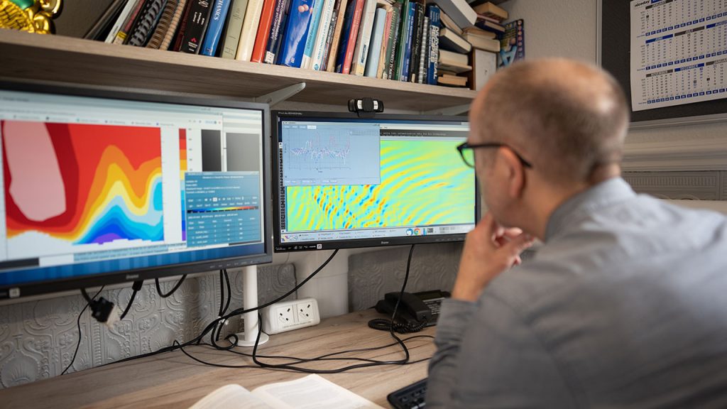 colourful weather model outputs on 2 computer screens with man in grey shirt