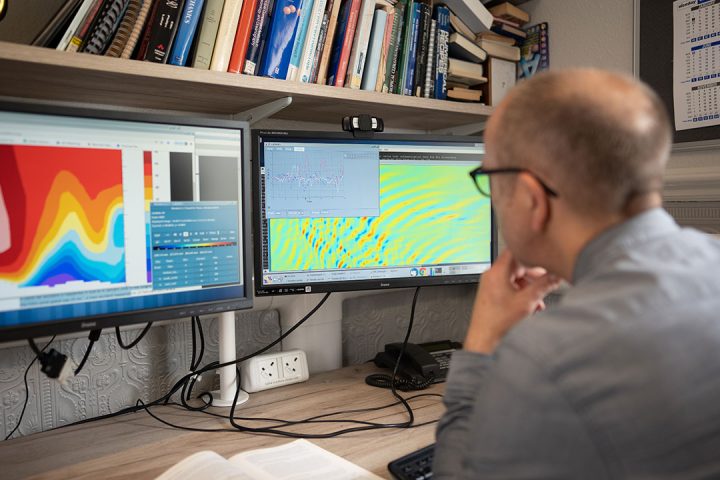 colourful weather model outputs on 2 computer screens with man in grey shirt