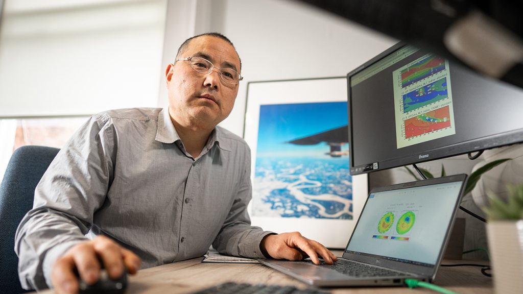 Person wearing grey shirt sits at desk with graphs displayed on two computer screens