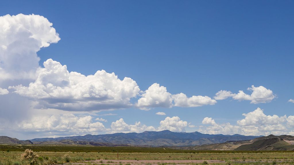 Fluffy, white clouds fill a blue sky above a mountain range