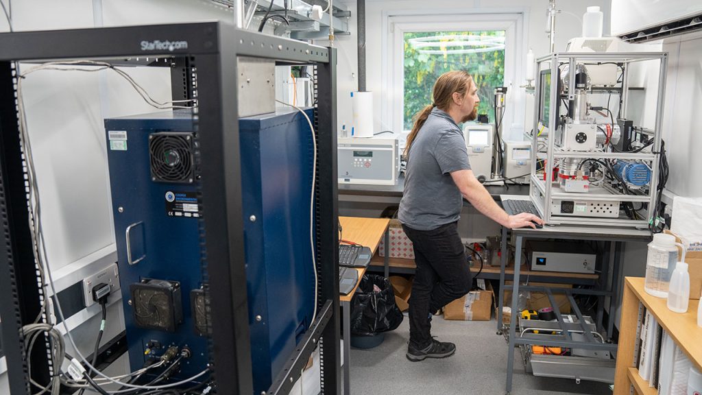 Dr James Allan stands at a computer in a laboratory space, surrounded by scientific instruments