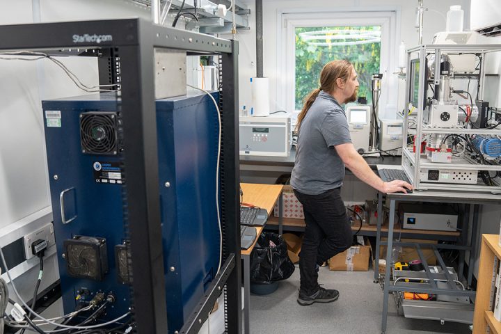 Dr James Allan stands at a computer in a laboratory space, surrounded by scientific instruments