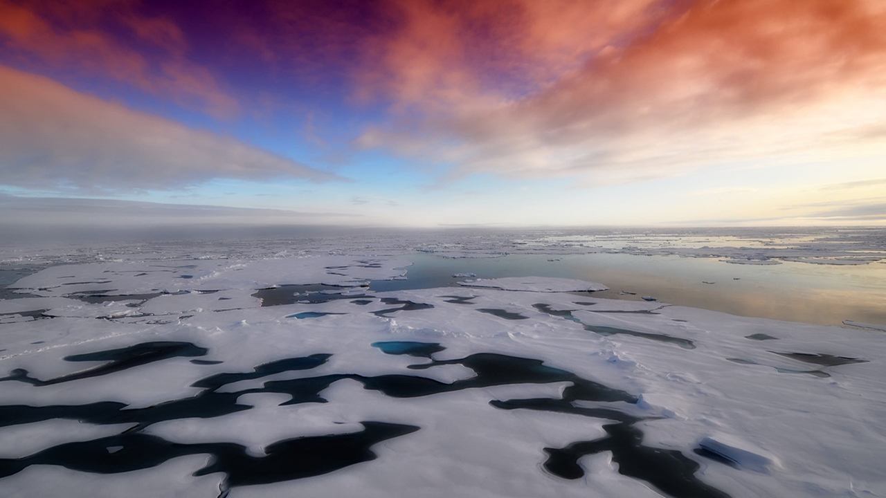 Patchy white ice over dark blue sea and a pink and bright blue sky