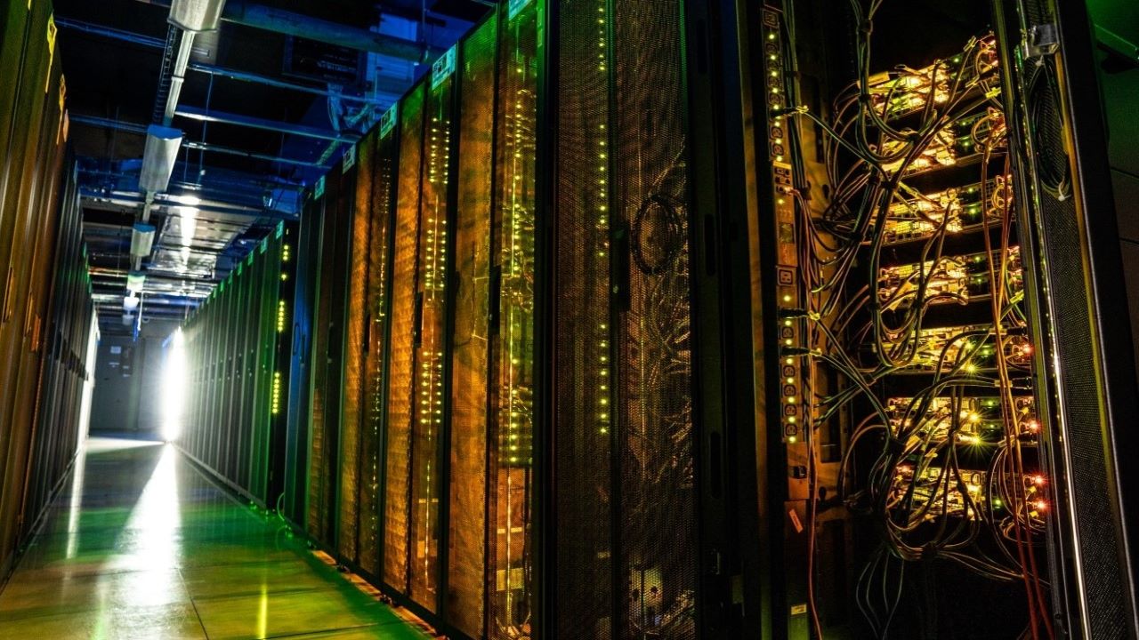 orange, green, and blue lights illuminate high power computing systems stored inside tall black mesh and metal cabinets