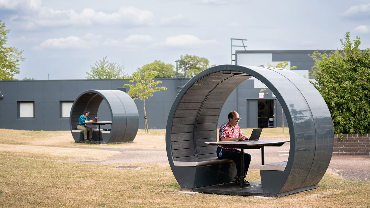 Two people sat in separate circular pods outside with green trees in the back.