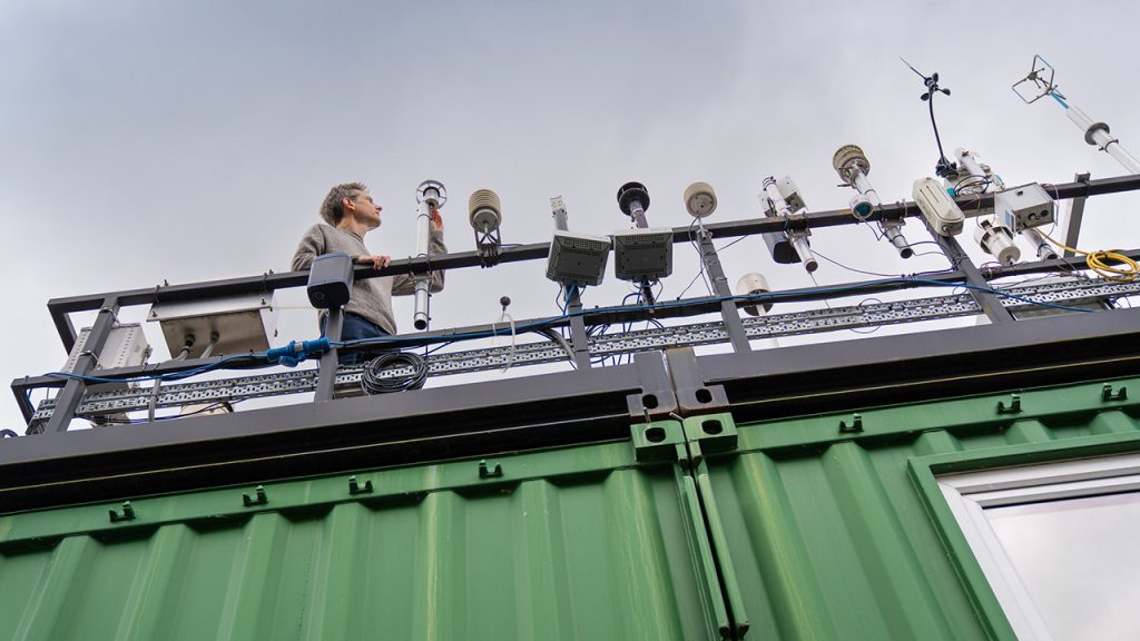 Person stands on top of green shipping container looking at a row of scientific instruments 