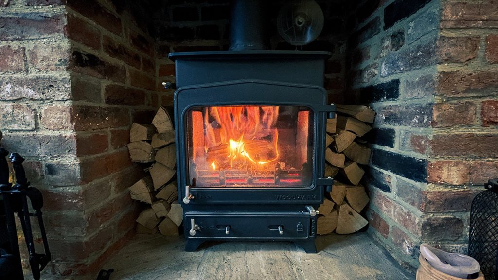 Log-burning stove in a brick fireplace with fire burning inside