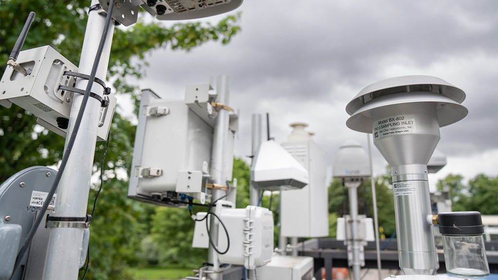 Array of white scientific instruments attached to upright metal poles on a rooftop observatory in a leafy, green suburb.