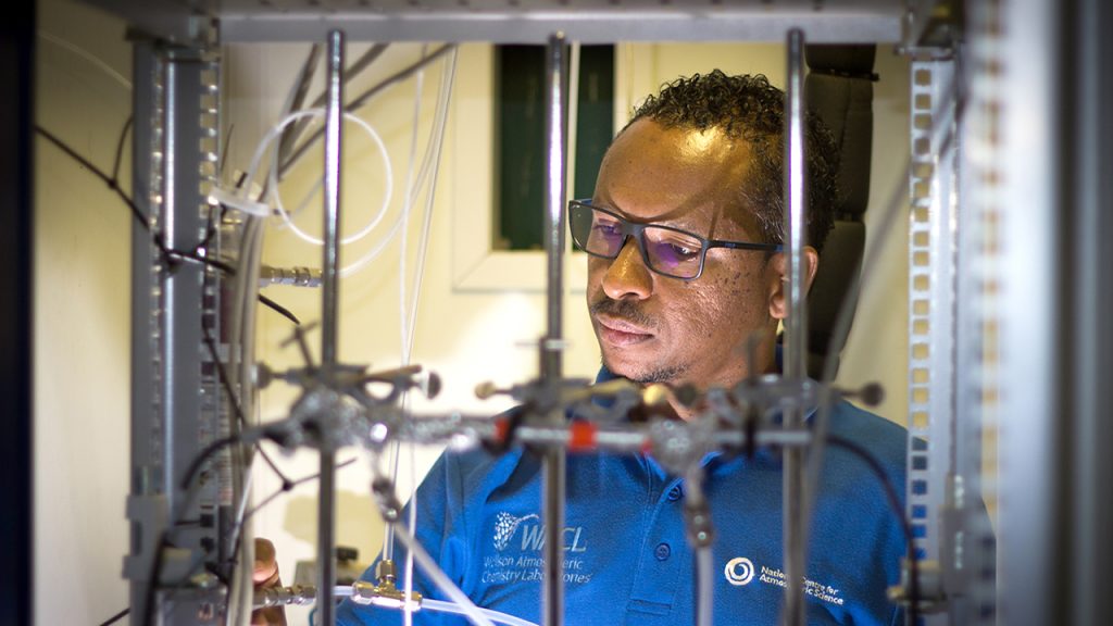 Person wearing glasses holds gas inlet tube in laboratory