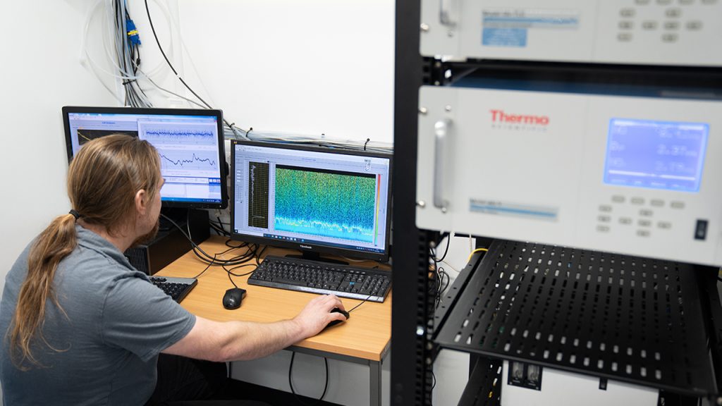 a person looking at data on two computer screens, with a black shelf next to them